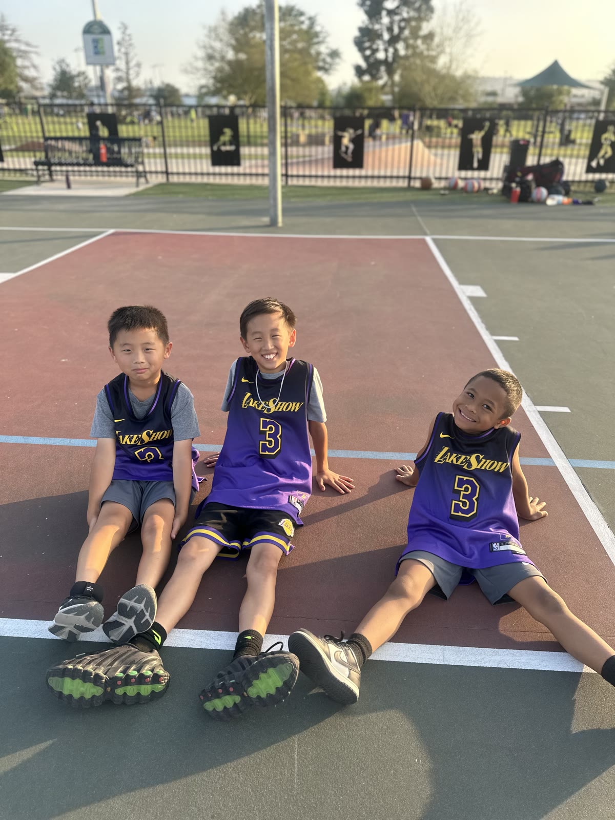 Three young basketball players sitting together on an outdoor court