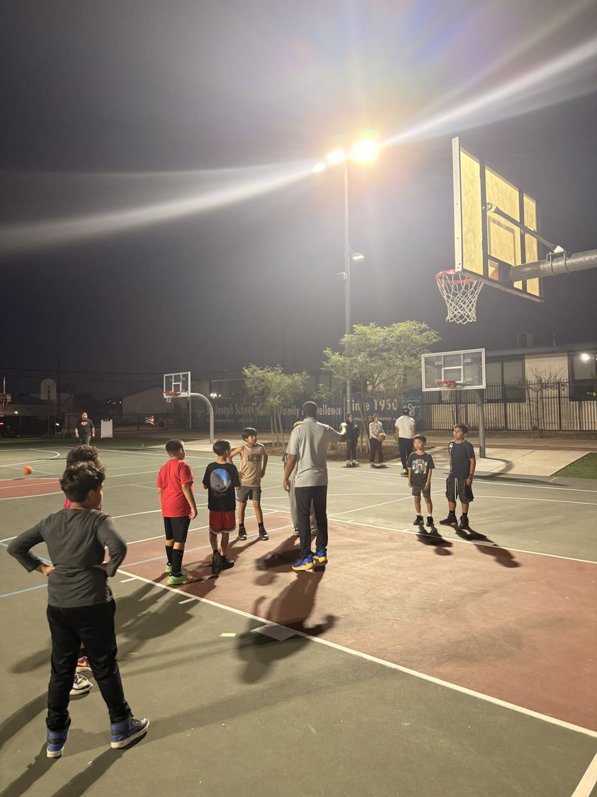 Young players gathered with a coach during an outdoor basketball practice at night