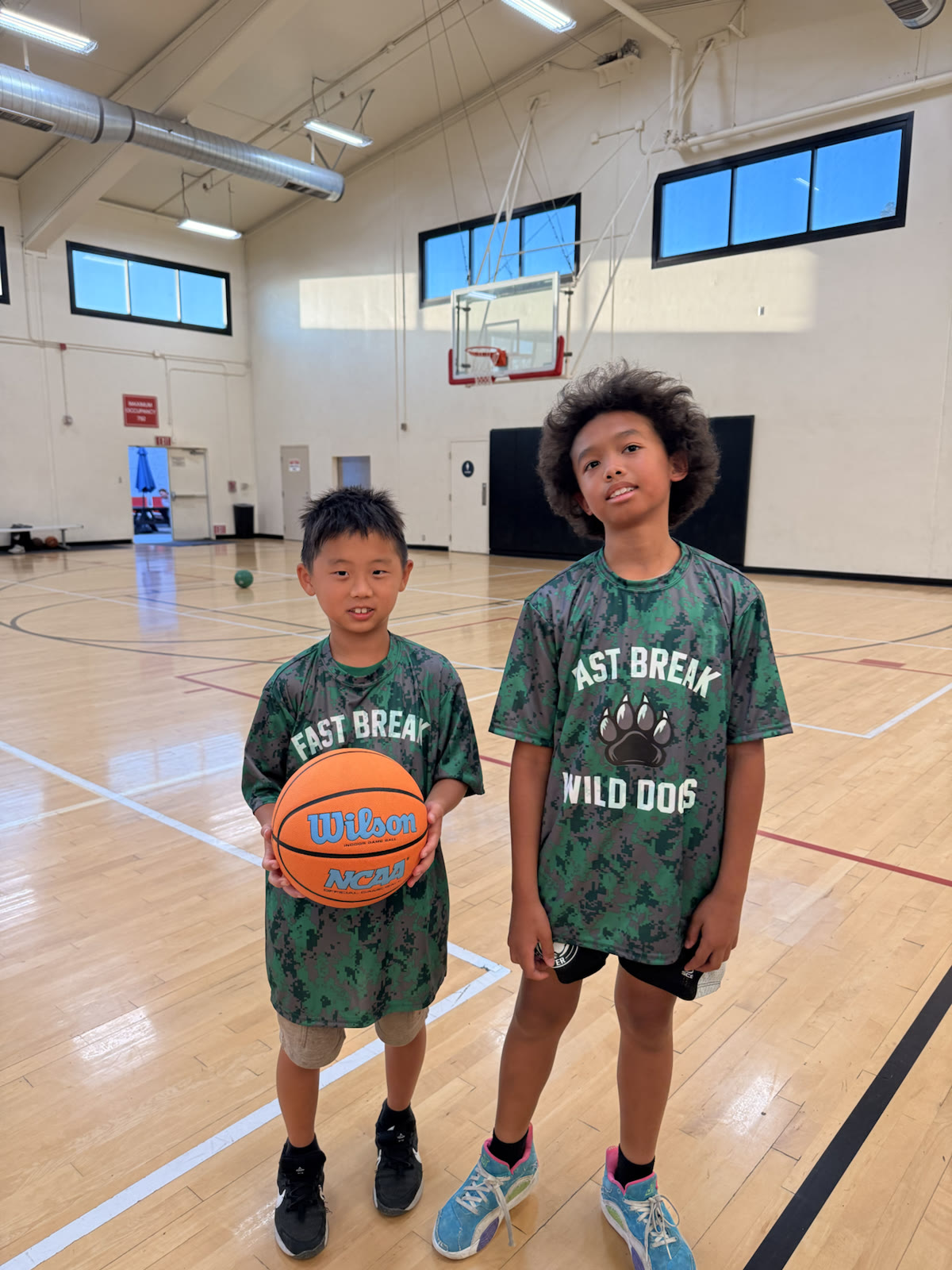 Two young basketball players wearing Fast Break Wild Dogs shirts in a gym